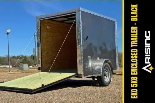 Open enclosed trailer with lime green interior floor, parked on gravel with desert landscape and clear blue sky visible