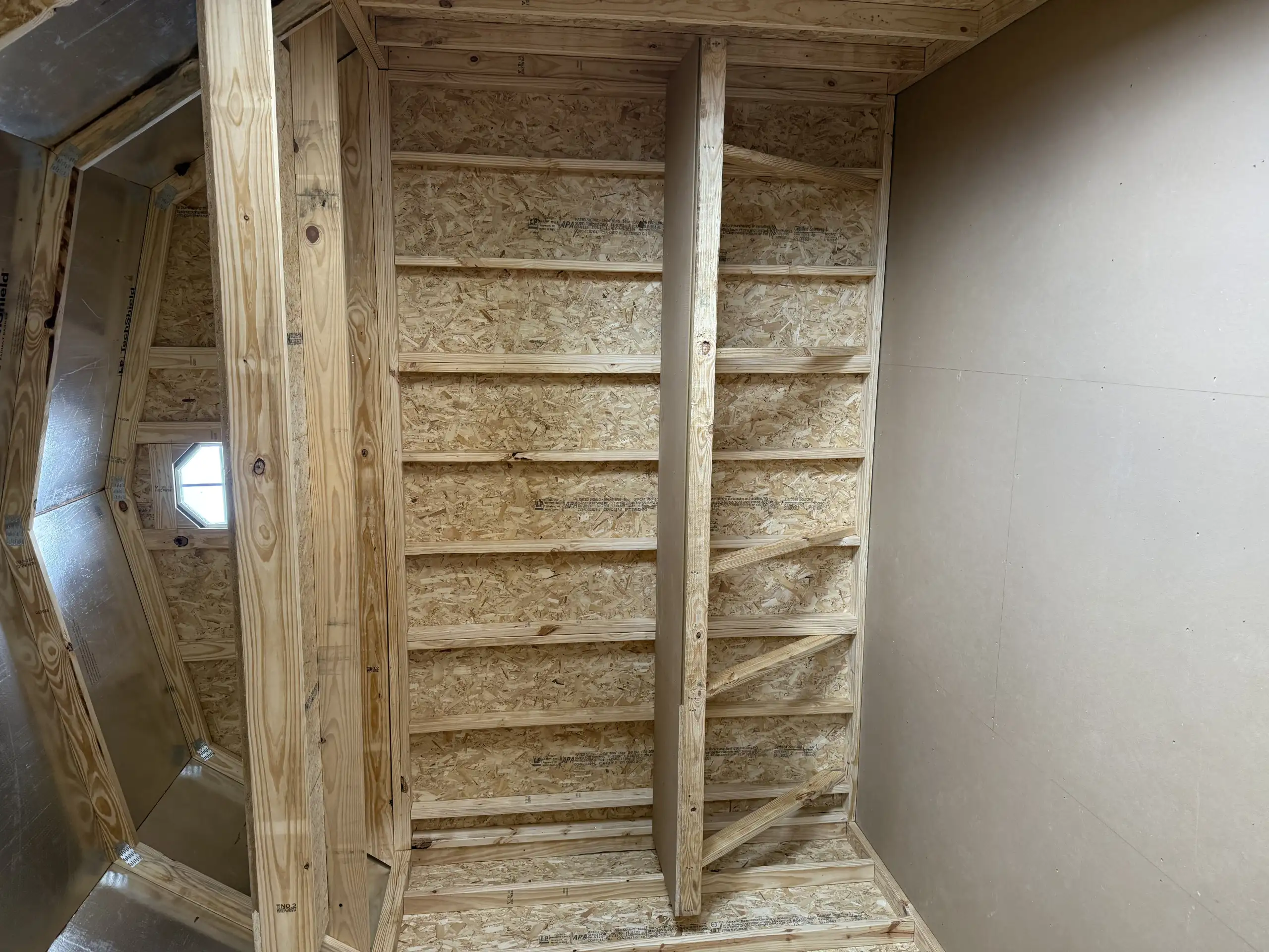Interior of an unfinished wood-framed shed showing two tall built-in shelf units made from OSB and pine lumber