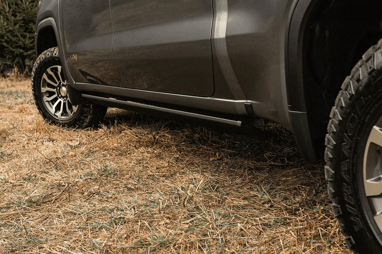 Black running board mounted below the side of a gray truck parked on a dirt driveway
