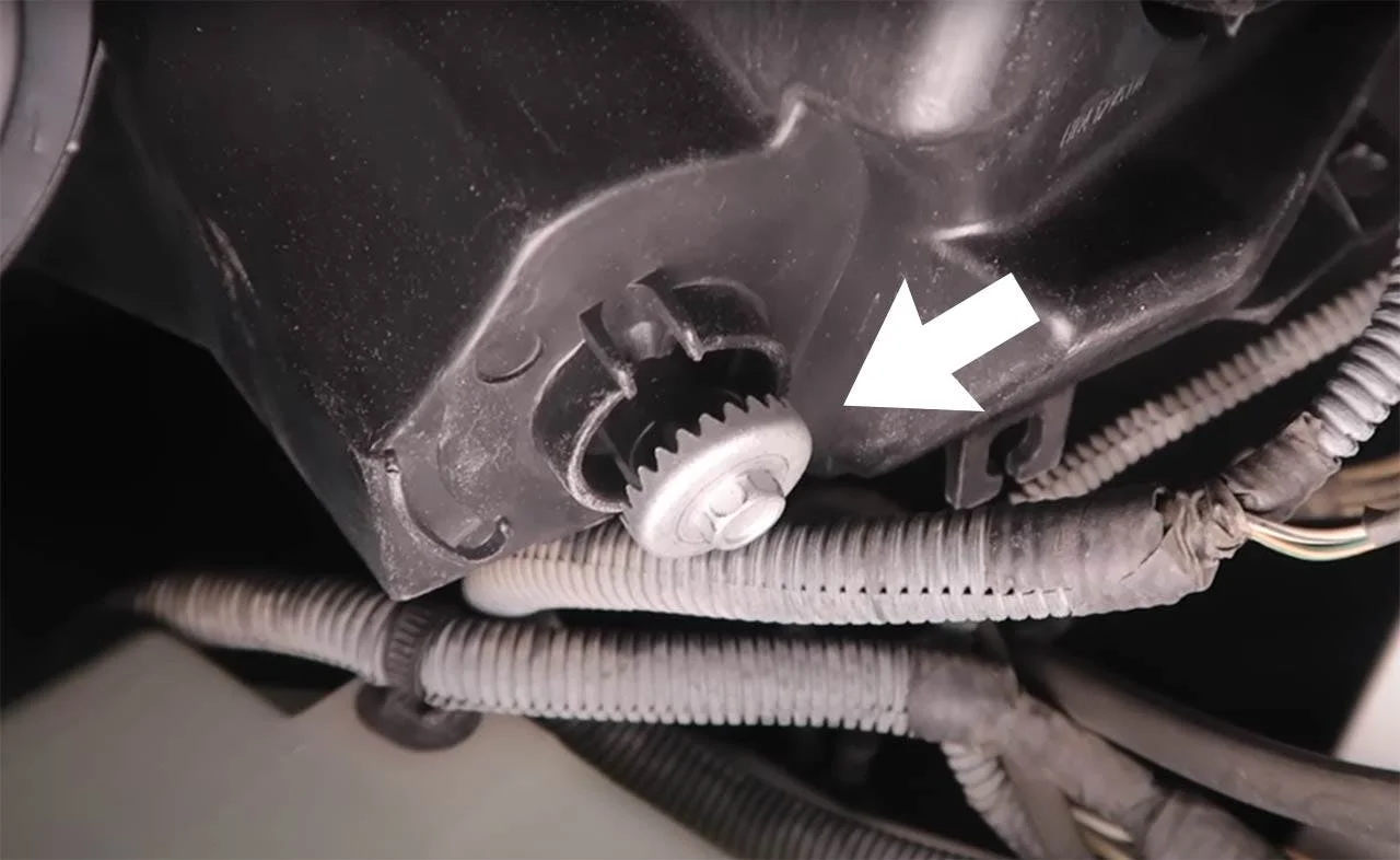 Adjustment bolt with white plastic cap and gear teeth visible on underside of truck headlight assembly