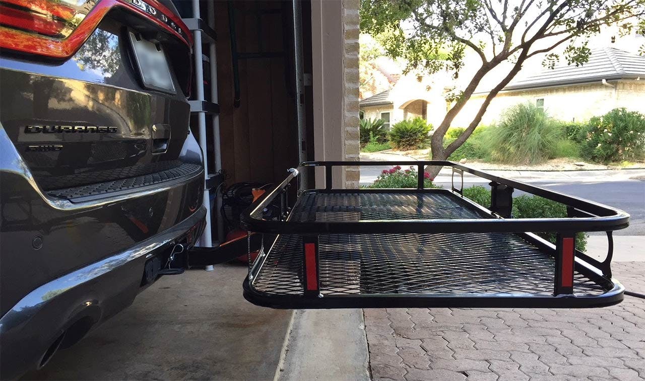 Black hitch-mount cargo basket with red supports attached to rear of dark truck in driveway