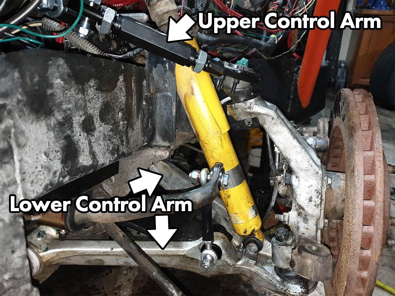 Yellow hydraulic cylinder connecting upper and lower control arms to the suspension on a truck wheel assembly