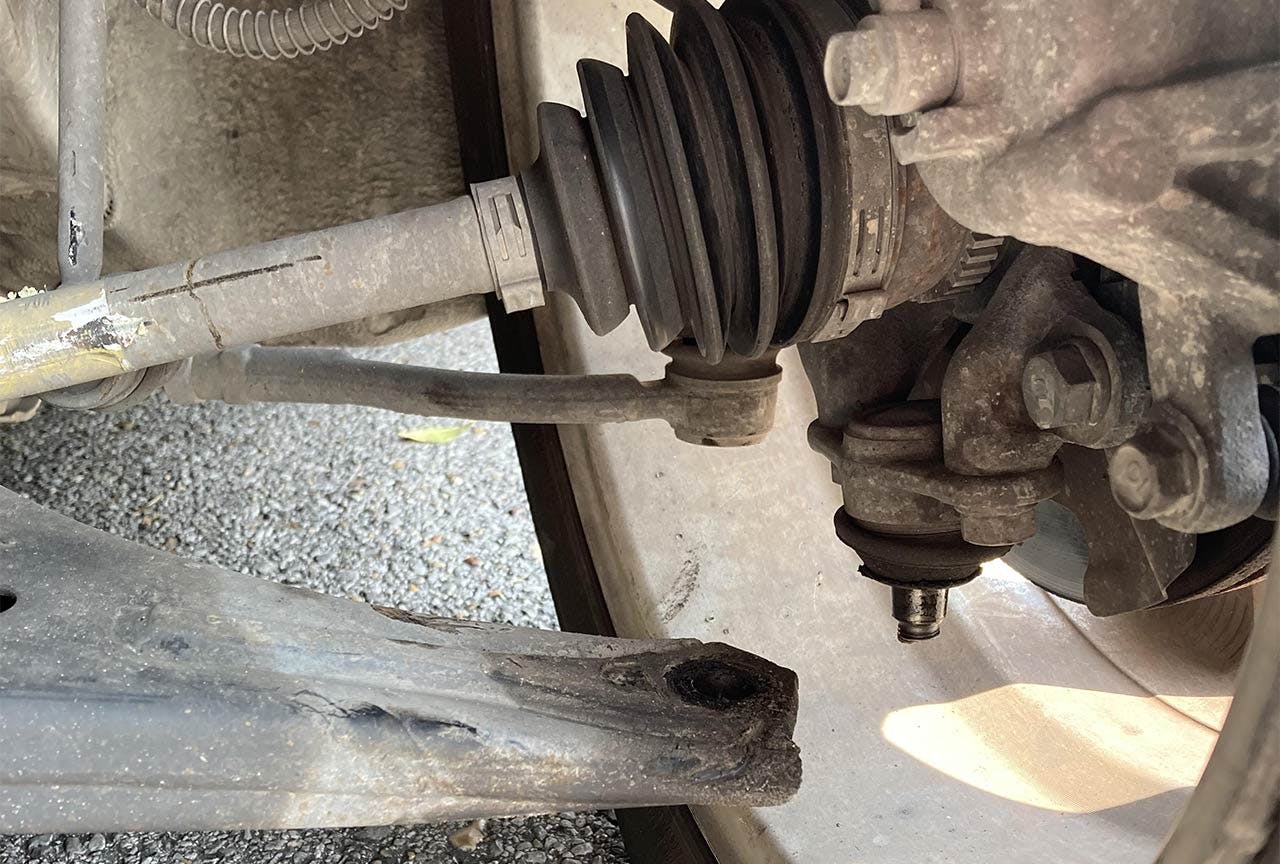 Truck control arm and ball joint assembly viewed from underneath, showing worn metal components and suspension hardware.
