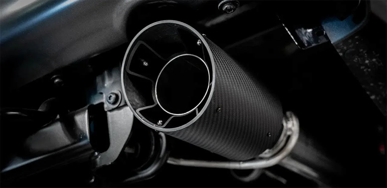 Carbon fiber exhaust pipe with polished metal end cap mounted on dark truck engine bay
