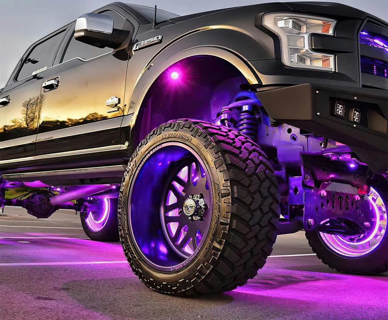 Lifted Ford truck with purple underglow lighting and illuminated wheel wells at night, showing custom suspension and