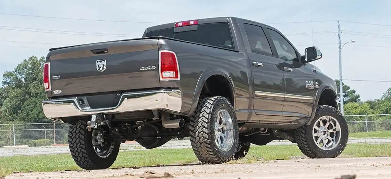 Brown pickup truck lifted on oversized off-road tires with chrome wheels parked on dirt lot