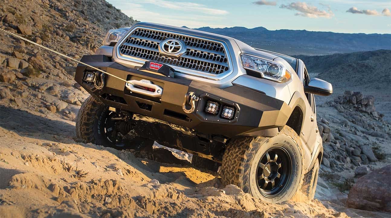 White Toyota truck with black front bumper and winch parked on rocky desert hillside overlooking mountains