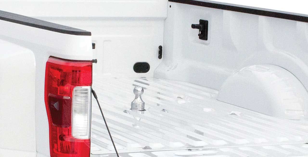 Empty white truck bed with red taillight on left side and chrome hitch ball mounted in center of bed floor