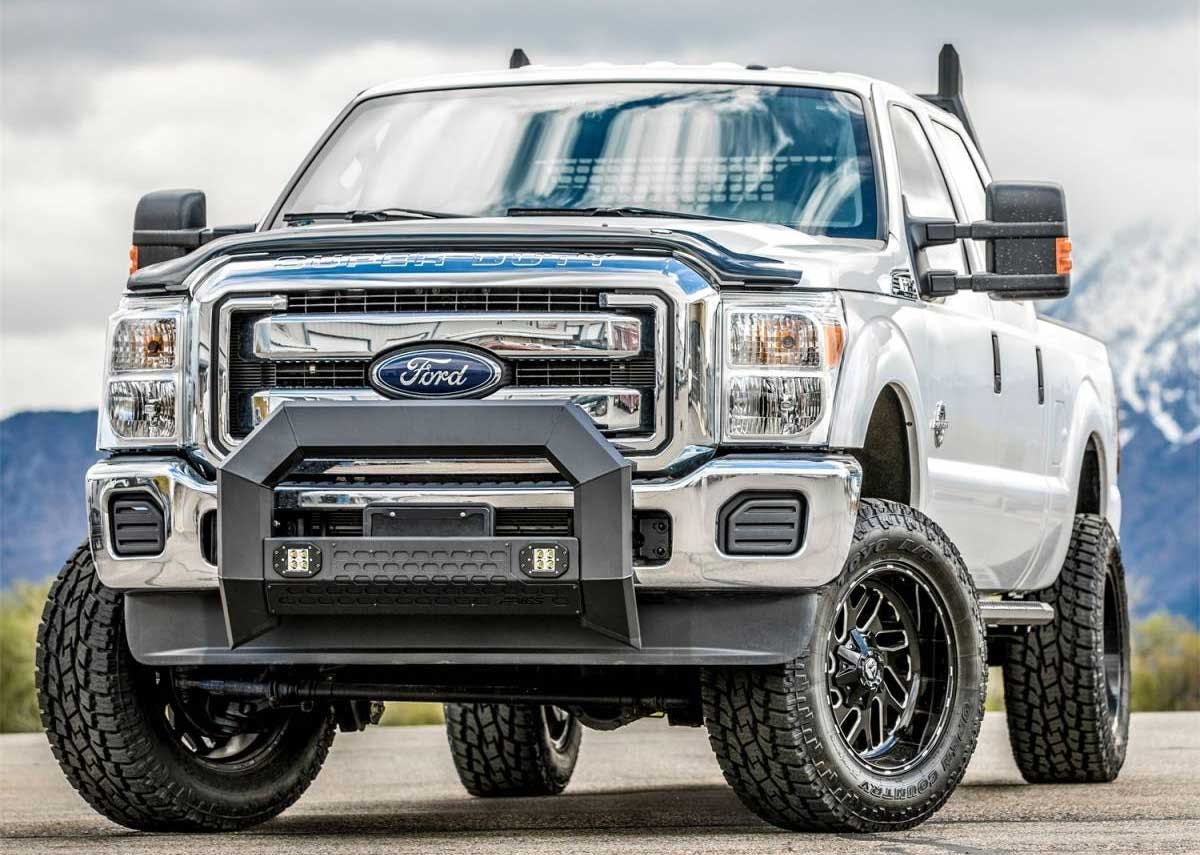 White Ford Super Duty pickup truck with black front bumper guard, LED lights, and all-terrain tires parked outdoors.
