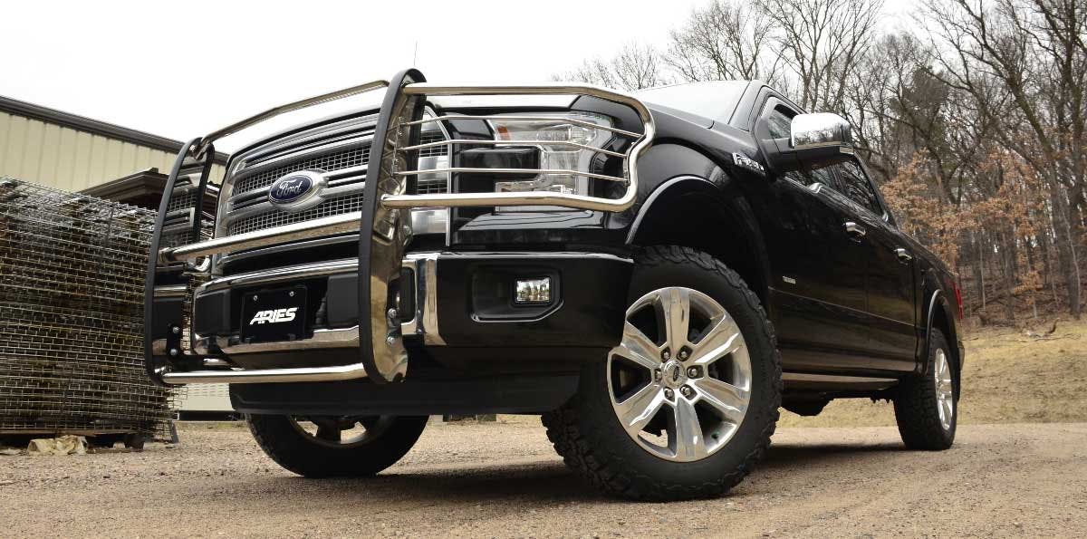 Black Ford Super Duty truck with chrome ARIES grille guard and bull bar parked on gravel near brick building.