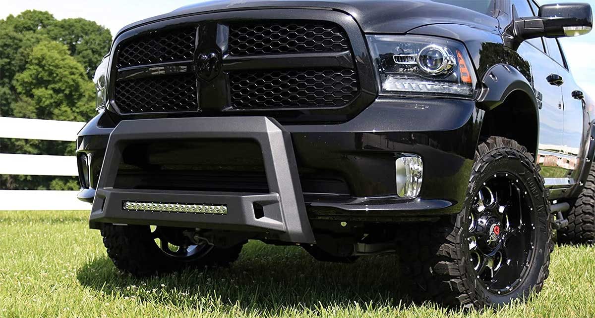 Black steel bull bar with integrated LED light bar mounted on front of truck in grassy field.