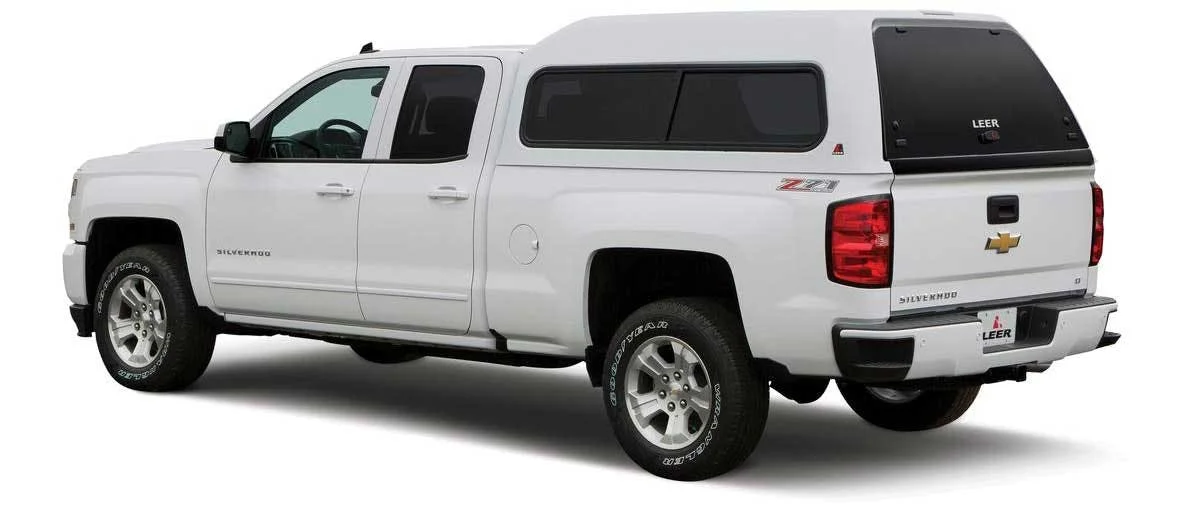 White Chevrolet Silverado pickup truck with a black LEER camper shell mounted on the bed, shown from the rear three-quarter