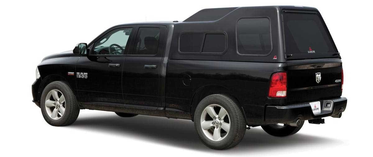 Black pickup truck with crew cab and LEER camper shell installed over the bed, shown from the side angle against white