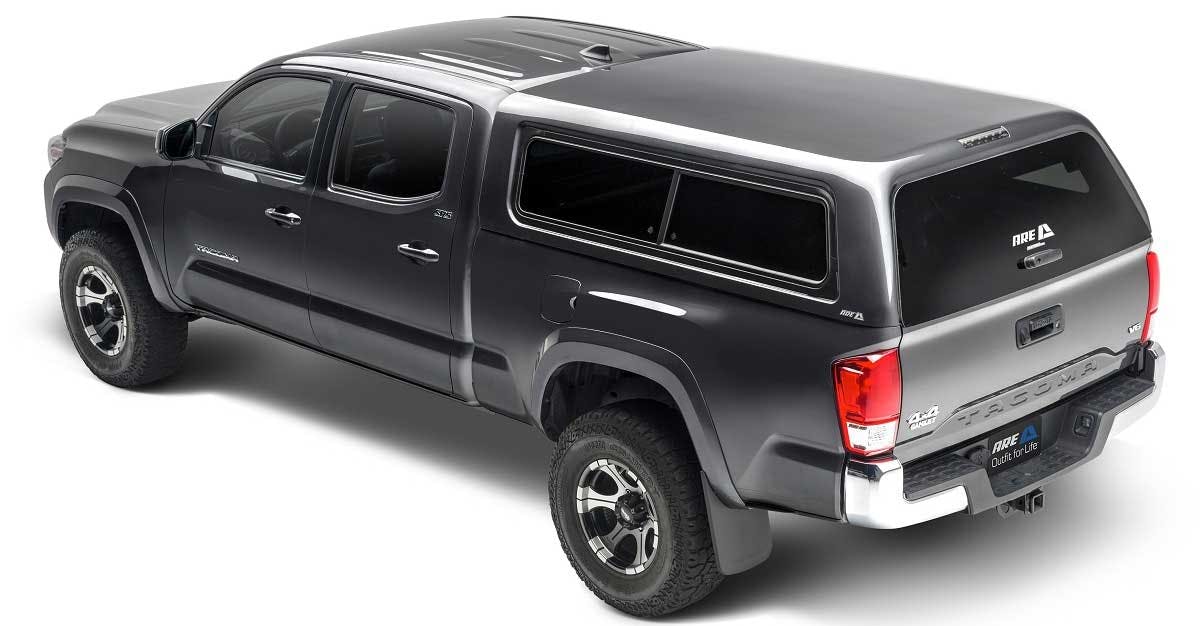 Black pickup truck with silver tonneau cover and dark-tinted canopy windows viewed from driver's side angle.