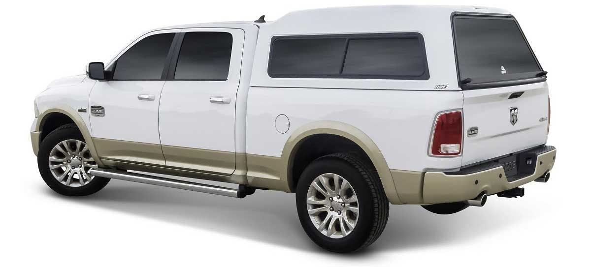 White and tan pickup truck with black camper shell featuring tinted rear windows, viewed from the side and rear angle.