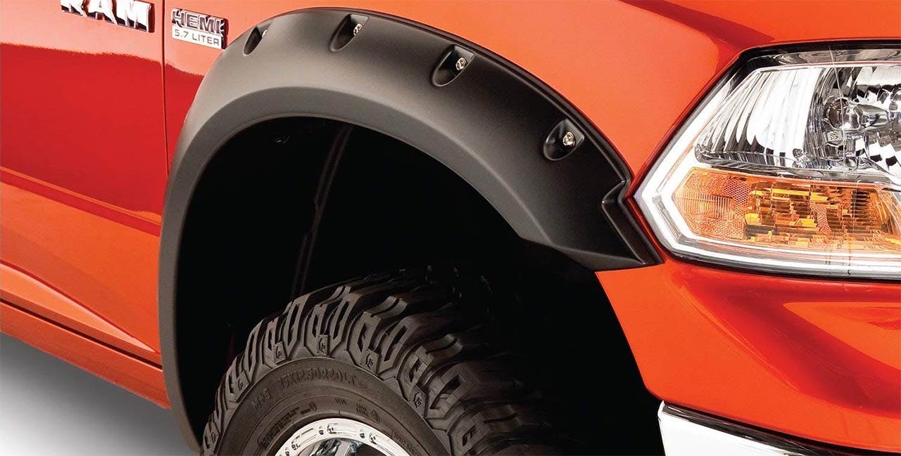 Black matte fender flare installed on orange truck wheel well with all-terrain tire visible inside