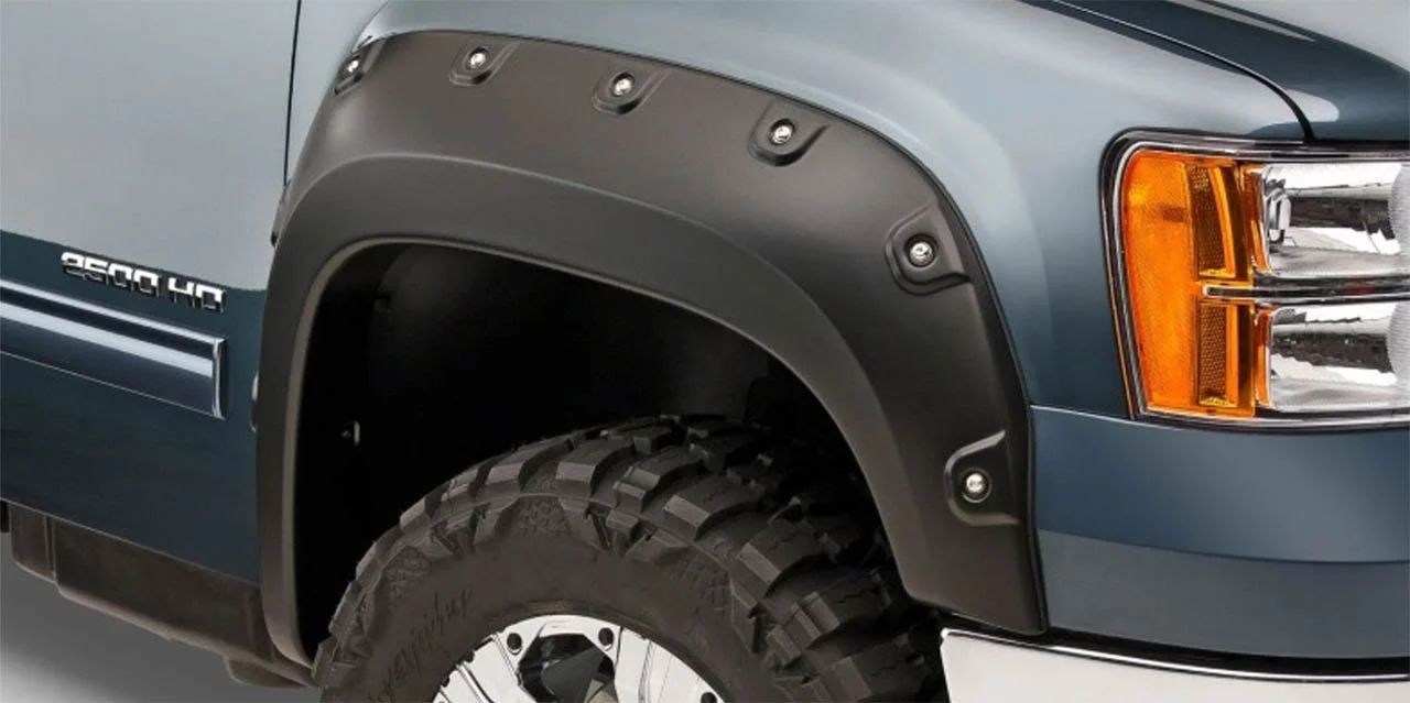 Dark gray bolt-on fender flare mounted on truck wheel well with visible metal studs, showing large black off-road tire