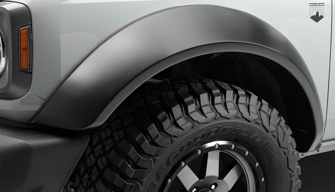 Close-up of a truck wheel with aggressive off-road tire and bolt-on fender flare on silver vehicle body