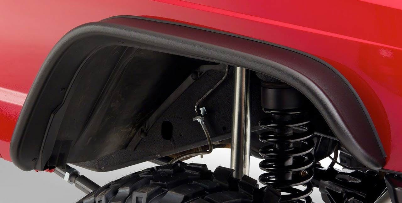 Black fender flare installed on red truck bed over coiled suspension spring and black tire