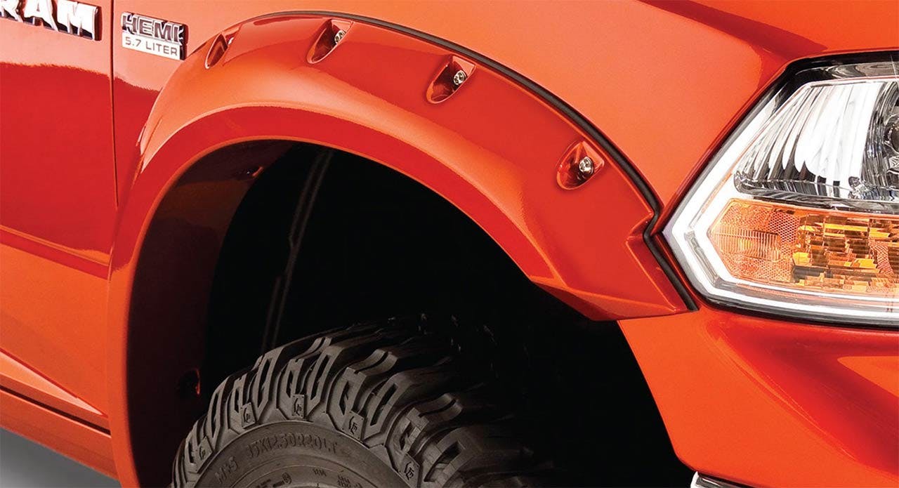 Red truck with open fender flare exposing an all-terrain tire with aggressive tread pattern in the wheel well