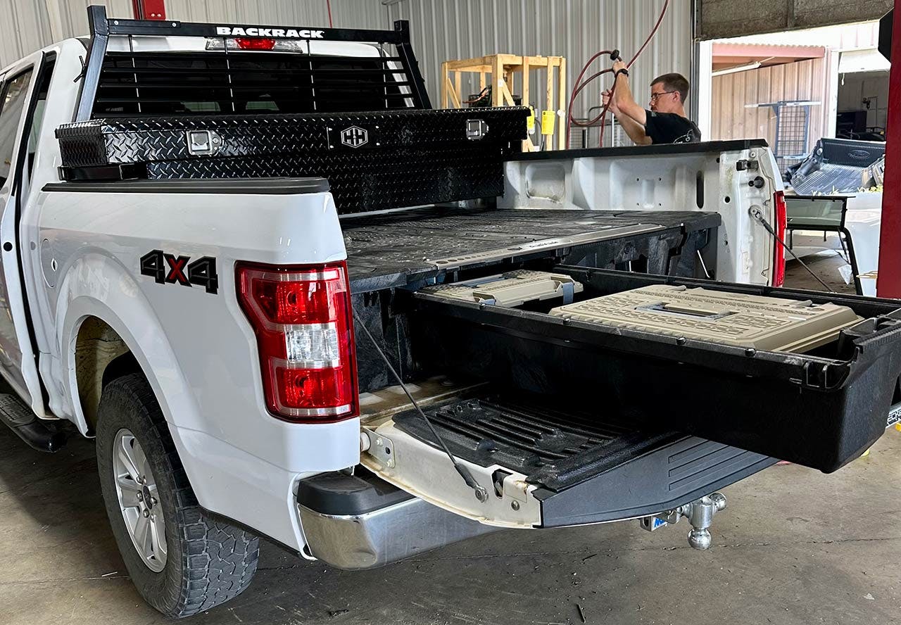 White 4x4 pickup truck with black headache rack mounted on cab and wooden sliding bed storage drawers in warehouse.