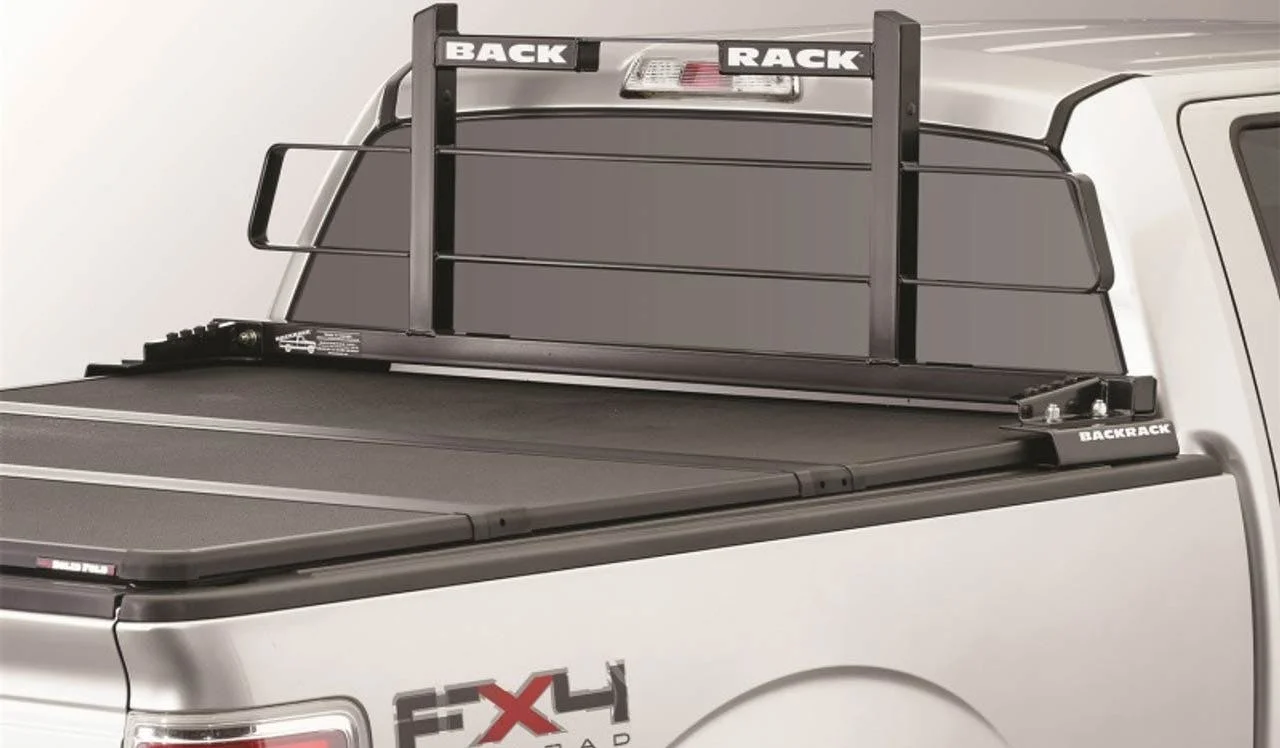 Black metal headache rack with horizontal bars mounted on white pickup truck bed behind cab, with tonneau cover visible below