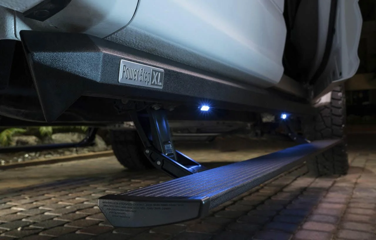 PowerStep XL electric running board extended beneath truck door with blue accent lighting on ground at night