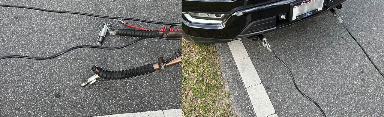 Tow bar components laid out on asphalt next to a black Ford truck, including coiled safety cables with red connectors and a