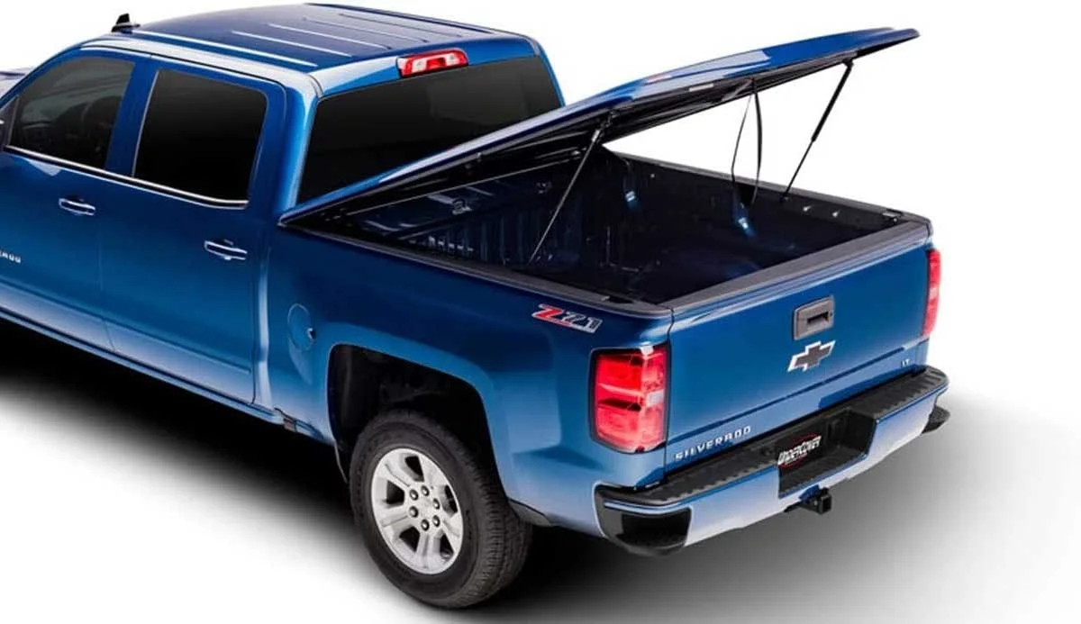 Blue Chevrolet Silverado with hard tonneau cover fully open, supported by gas struts, revealing empty truck bed