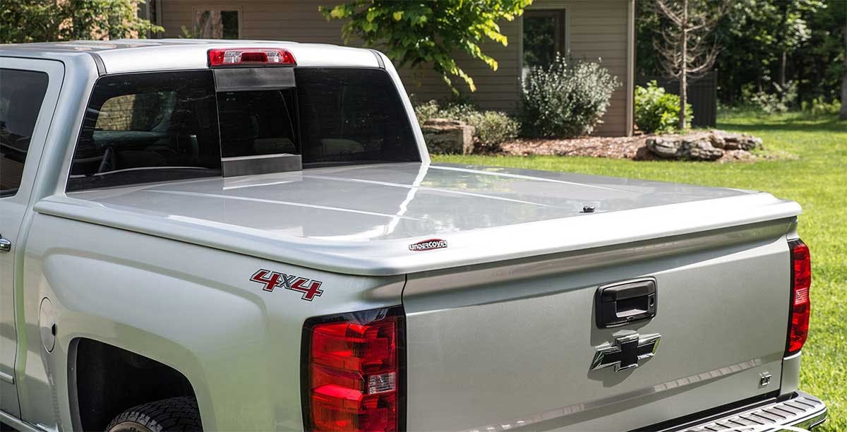 White hard tonneau cover on silver pickup truck bed in residential driveway with landscaping