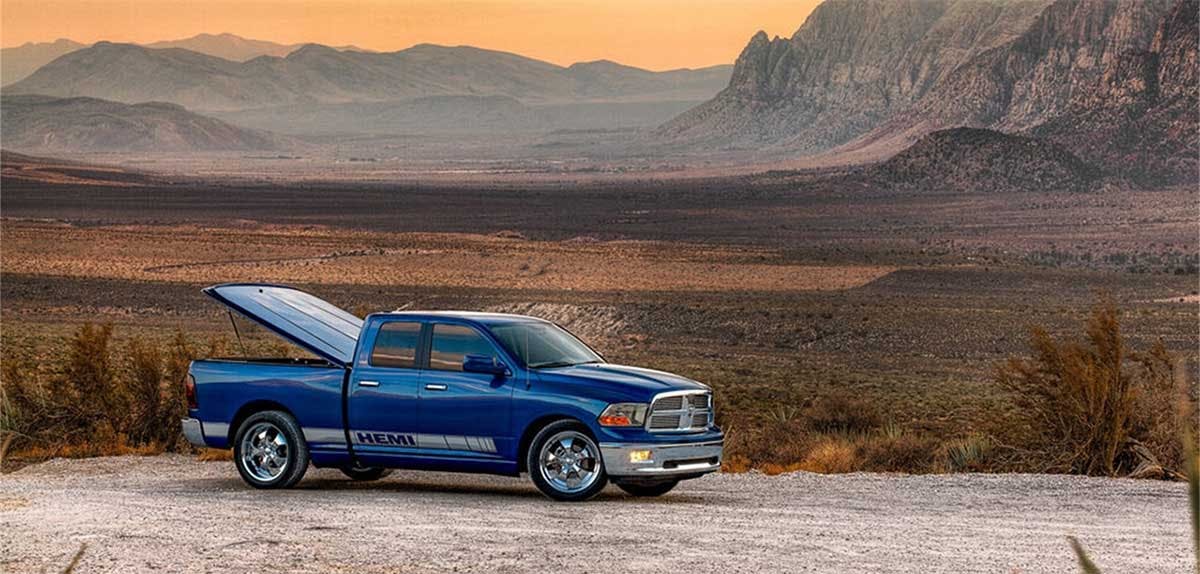 Blue pickup truck with open hood parked in desert landscape with mountains in background
