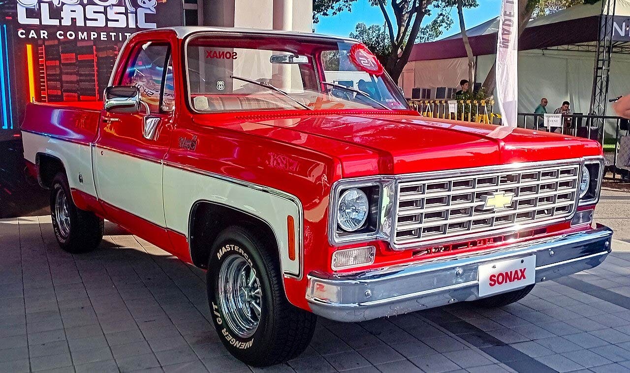 Red and white 1970s Chevrolet pickup truck with chrome grille displayed at outdoor car show event