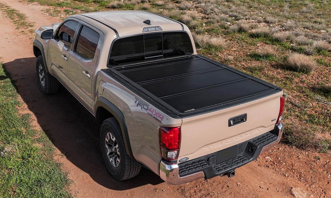 Tan Ford Raptor with black retractable tonneau cover extended over truck bed on dirt lot