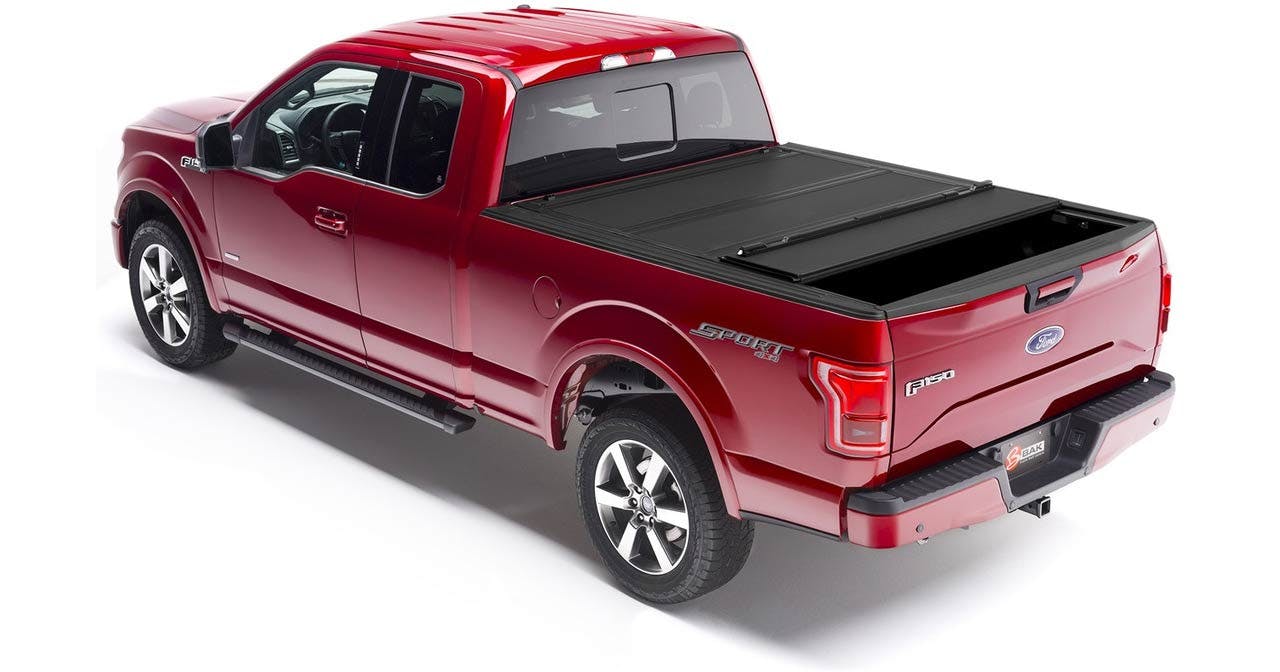 Red Ford F-150 pickup truck with open black tonneau bed cover partially rolled back, showing truck bed interior