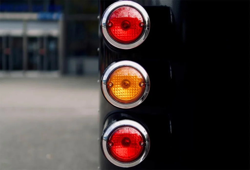 Red and amber round tail lights with chrome bezels mounted vertically on black truck panel.
