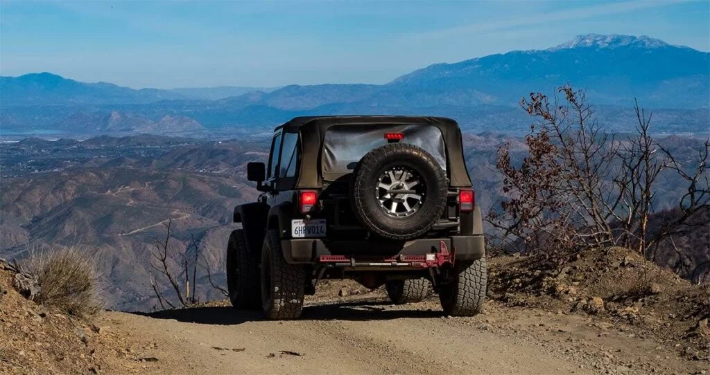 Black Jeep Wrangler parked on dirt mountain overlook with snowy peaks and desert valley visible in background