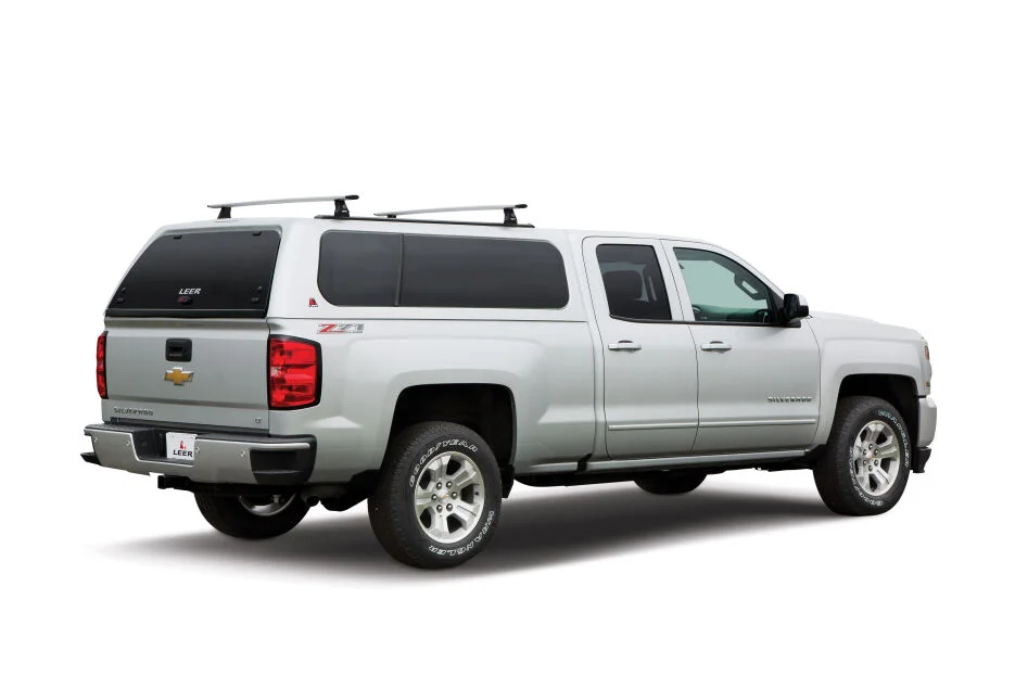 LEER 100XL truck cap with roof rack crossbars on a silver Chevrolet Silverado Z71, rear three-quarter driver side