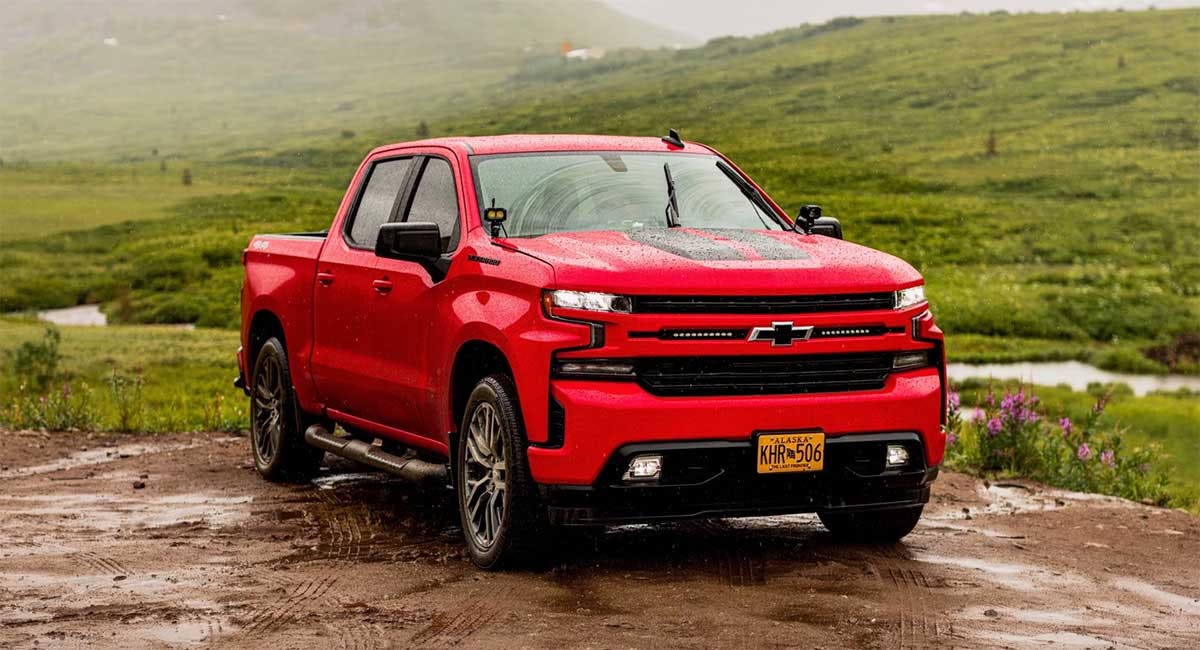 Red Chevrolet Silverado pickup truck parked on muddy ground with rolling green hills in background