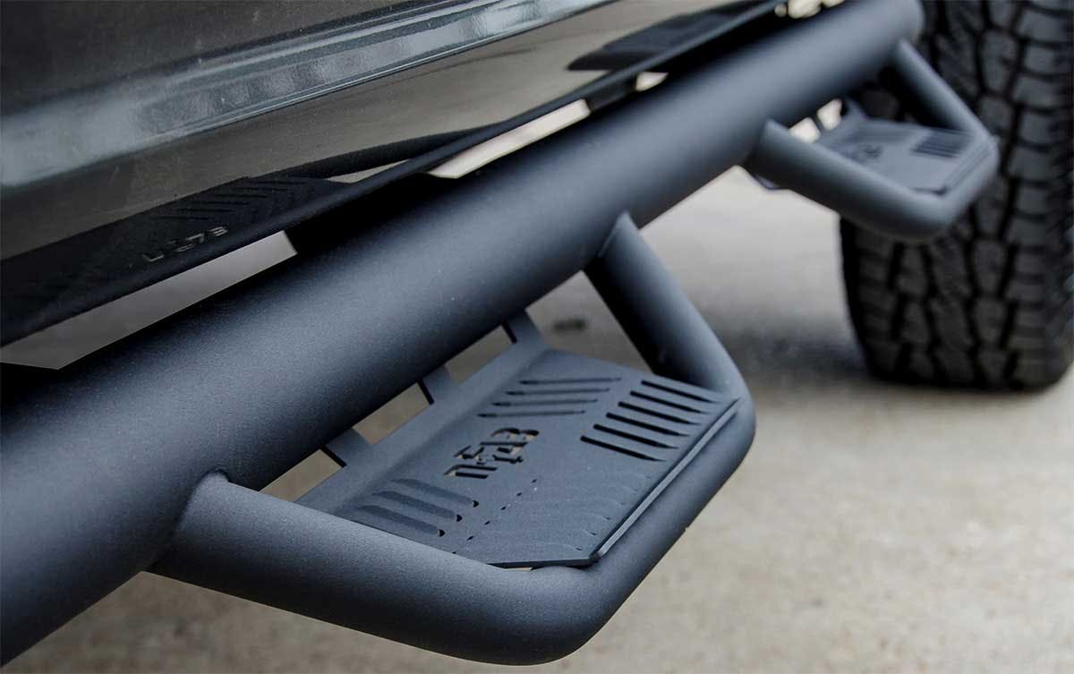 Black tubular nerf bar mounted on truck side with textured step platform and drainage vents.