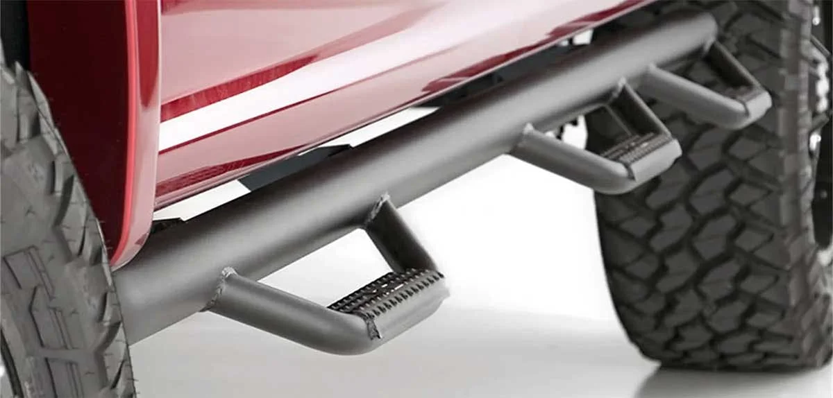 Black nerf bar with textured grip step mounted under red truck door, shown from side angle near tire.