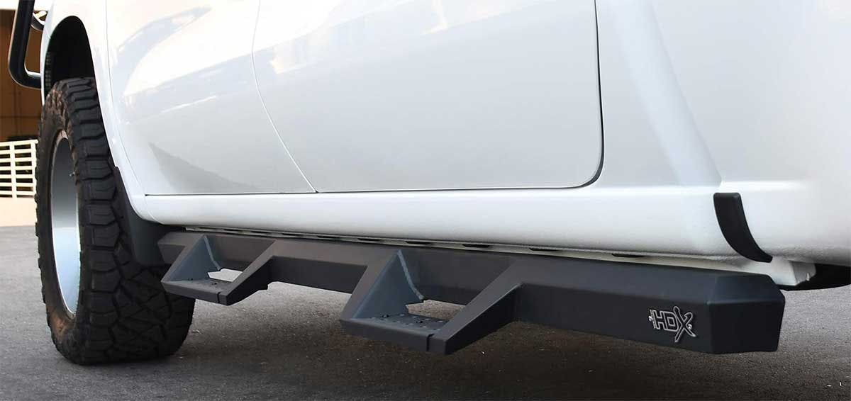 Black nerf bars mounted under the side of a white truck, providing a step for vehicle access.