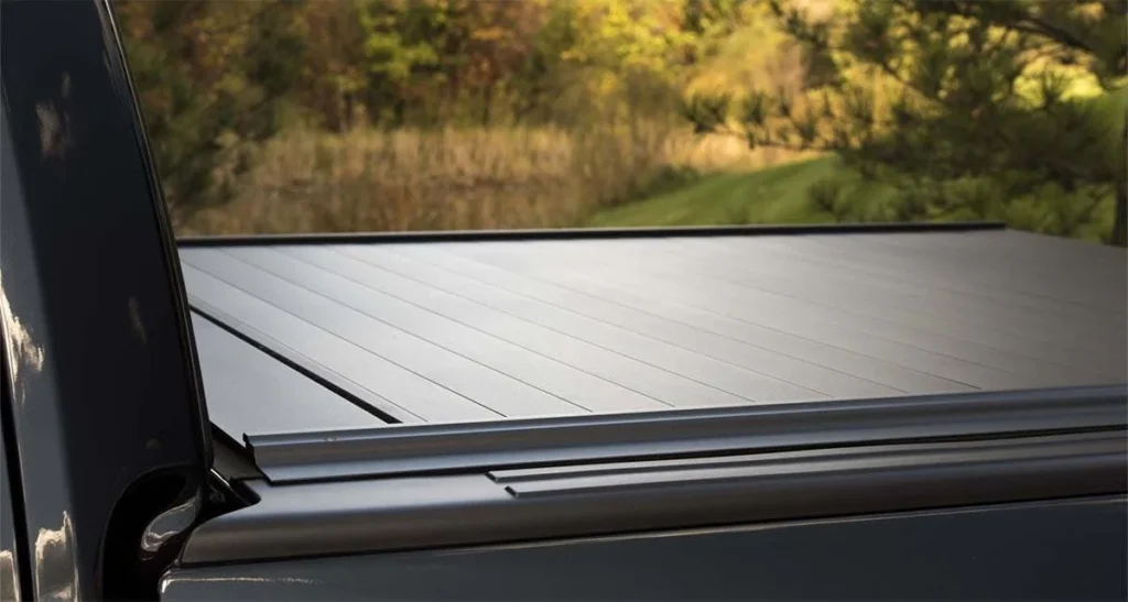 Closed aluminum tonneau cover on truck bed with forested landscape visible behind it