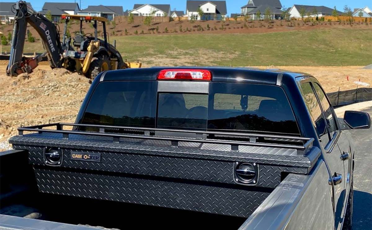 Black diamond-plate tool box mounted in the bed of a blue pickup truck at a construction site
