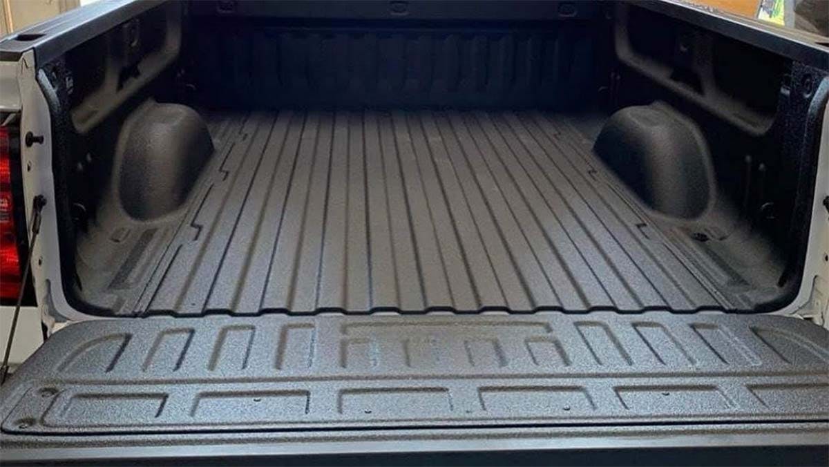 Empty pickup truck bed with black spray-on liner coating and round storage compartments on each side