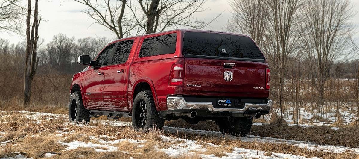 Red Dodge Ram 1500 pickup truck parked in a field with bare trees and patches of snow on winter ground