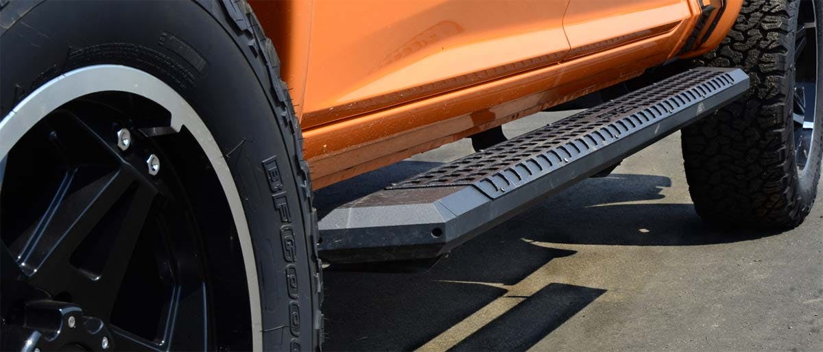 Black textured side step running board mounted on orange truck bed, viewed from ground level.