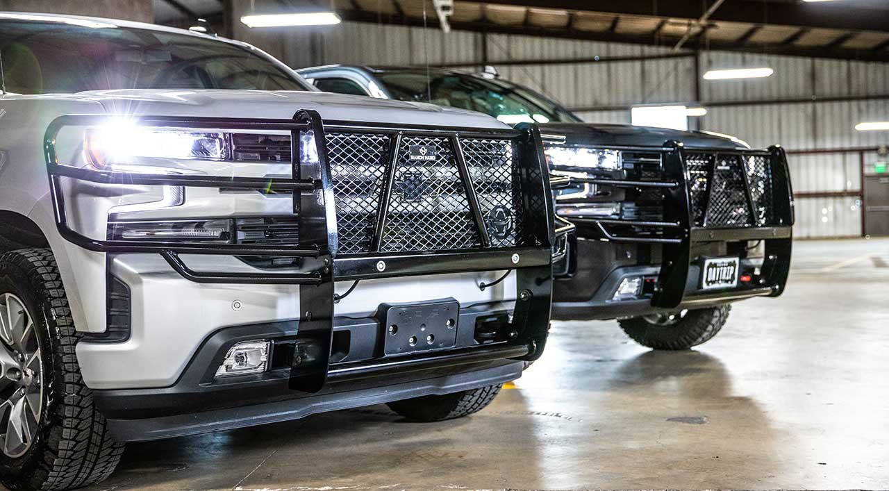 Row of trucks parked in warehouse with black steel ranch-style bumpers and mesh grilles installed on front ends