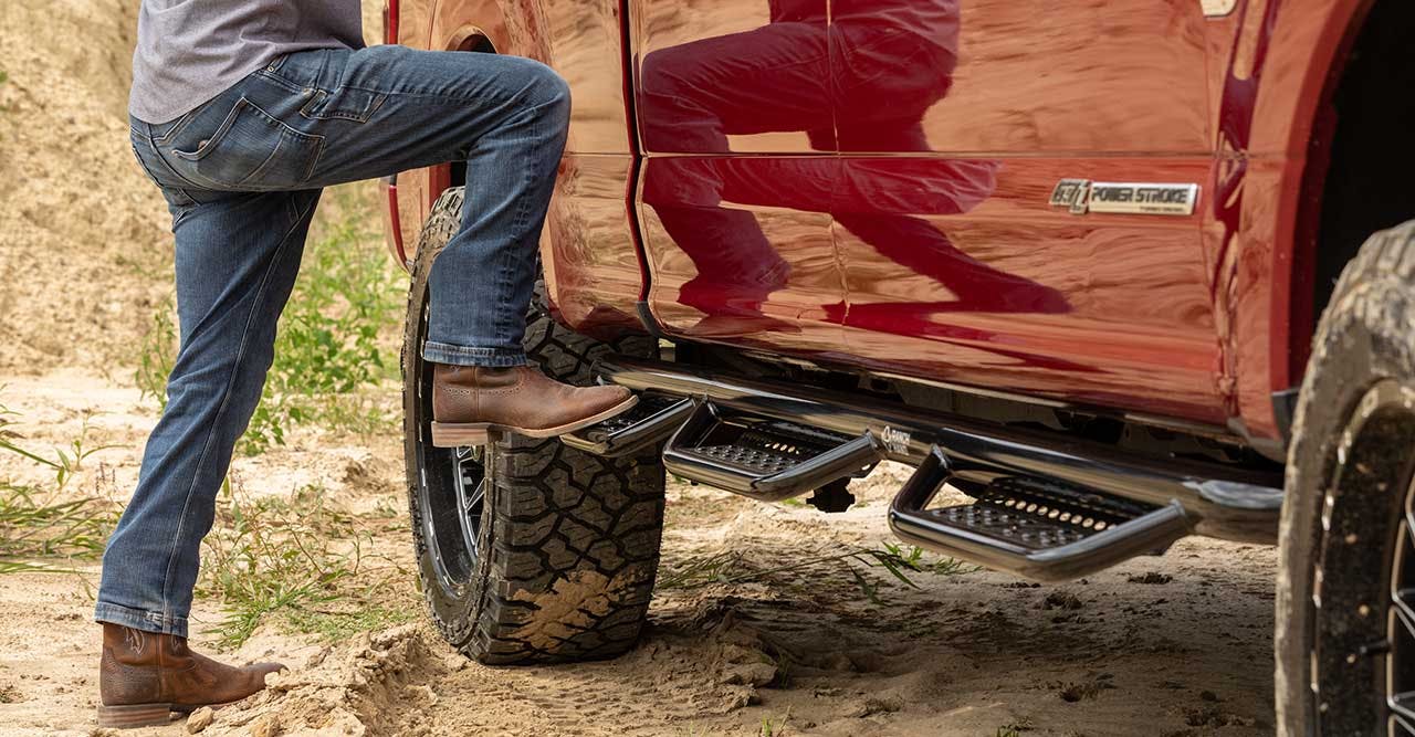 Person stepping onto truck running board with boot, red pickup truck visible with metal step below door
