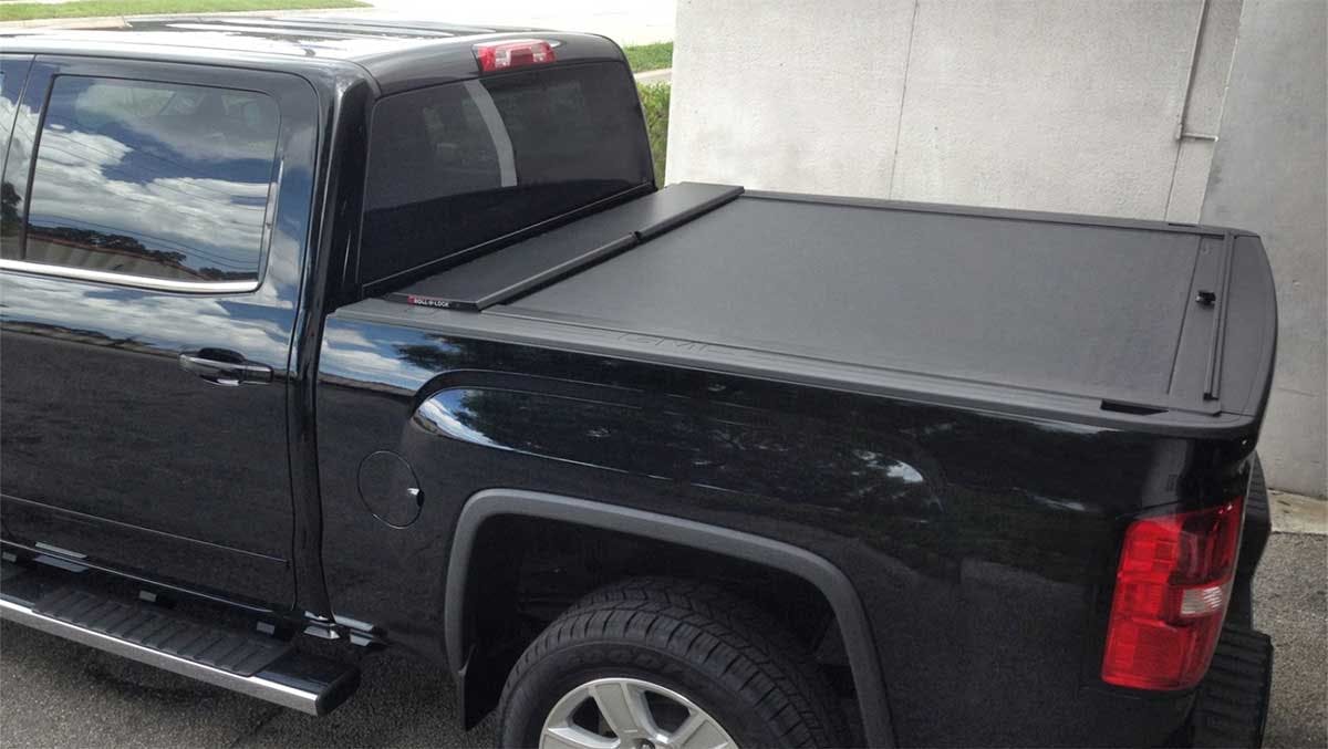 Black pickup truck with retractable tonneau cover rolled back over the bed, parked against a concrete wall