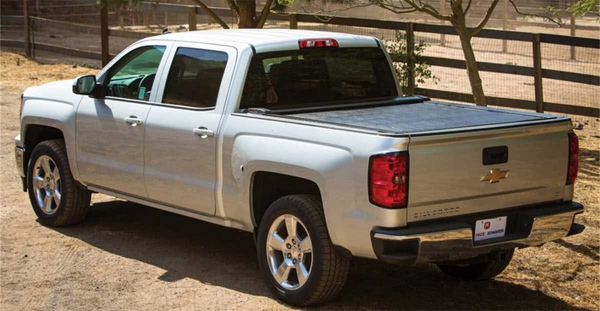 White Chevrolet Silverado pickup truck with closed metal tonneau cover over bed, parked near wooden fence.
